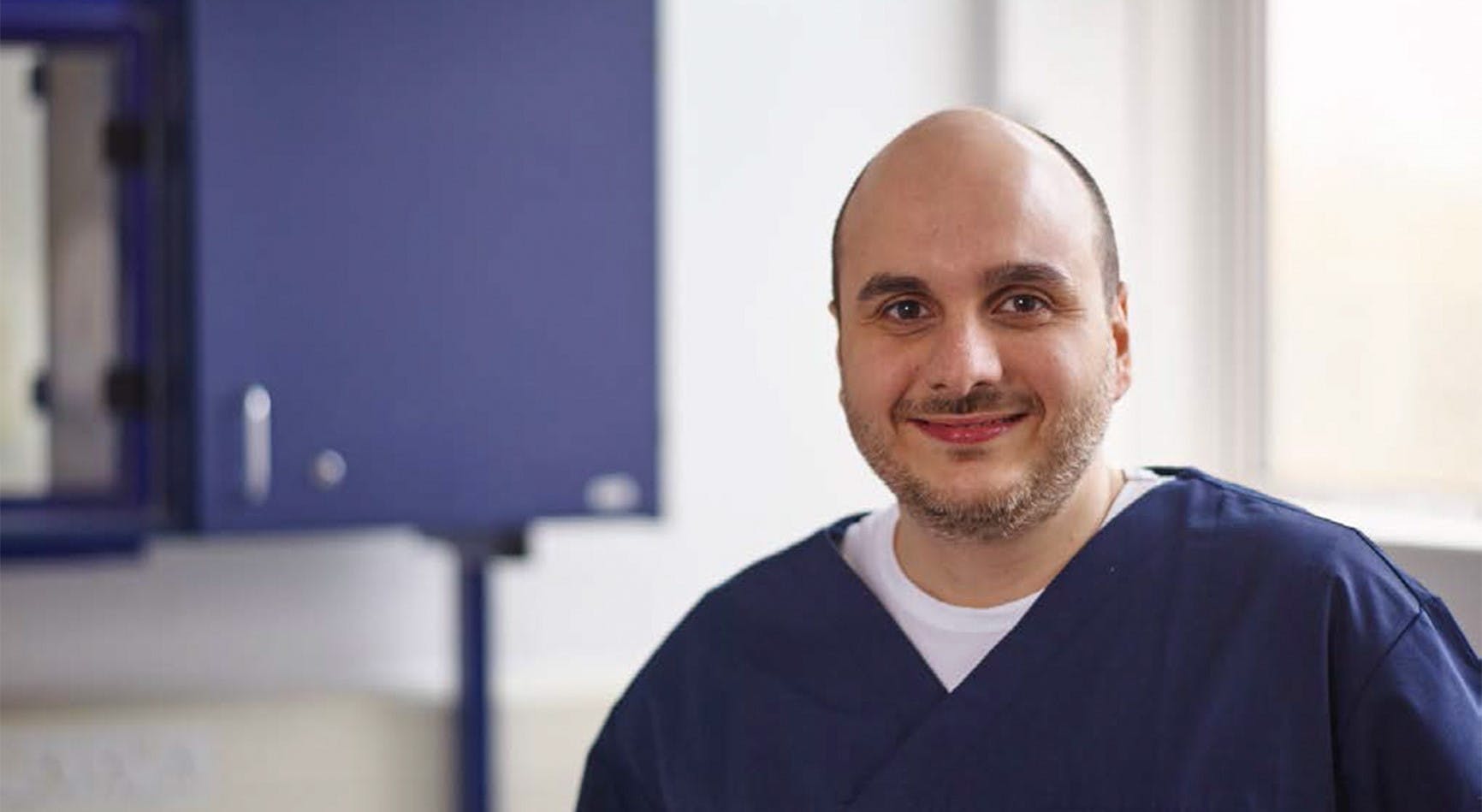 Dentist dressed in scrubs smiles directly at camera