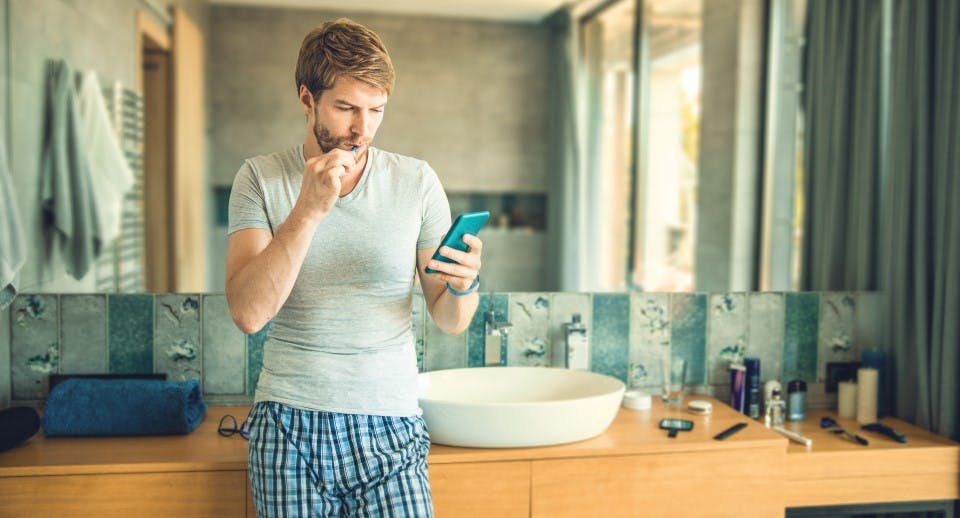 A man brushing his teeth and looking at his phone