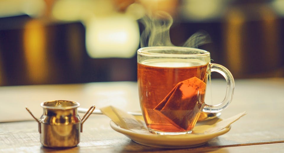 A steaming hot glass mug of tea on a table