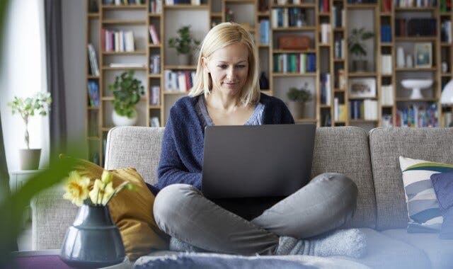 Woman sitting cross-legged on her couch while reading  something on her computer