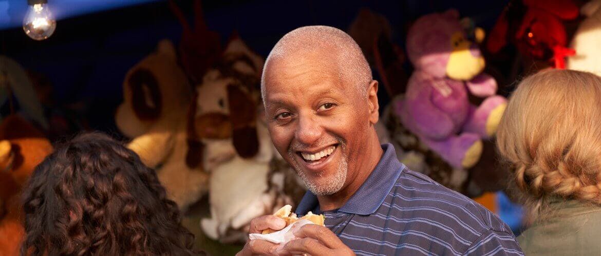 Smiling man holding a partly eaten burger at a town carnival