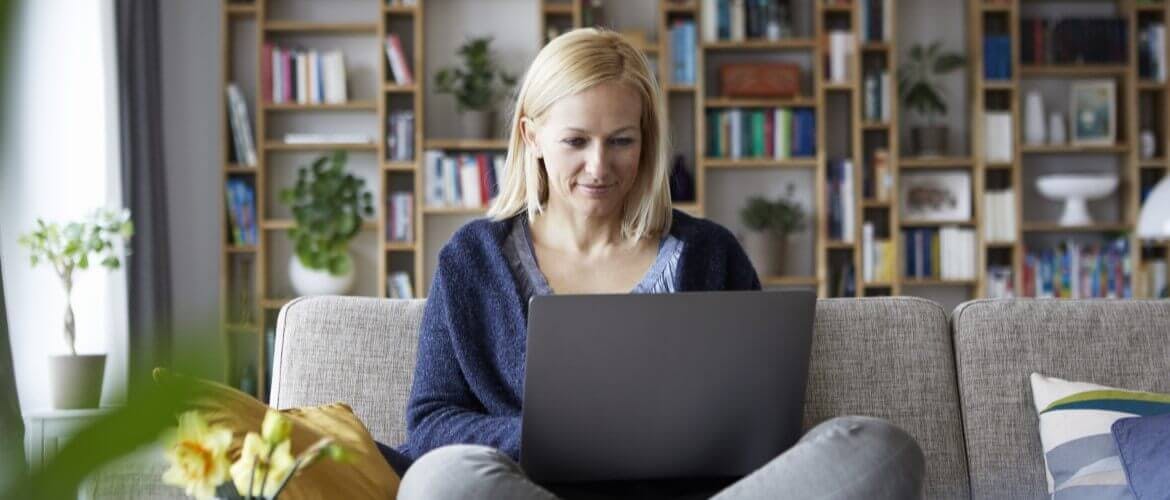 Woman sitting cross-legged on her couch while reading  something on her computer