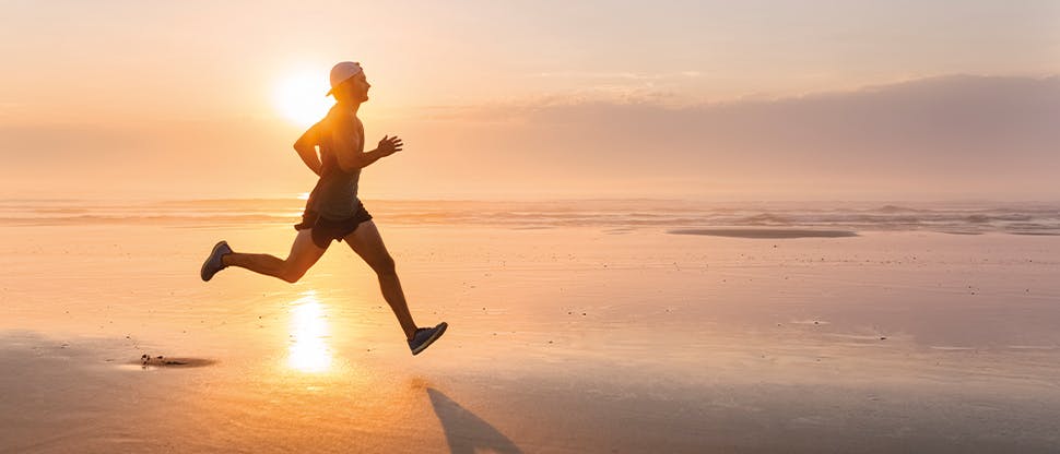 Muž běžící po pláži při západu slunce
