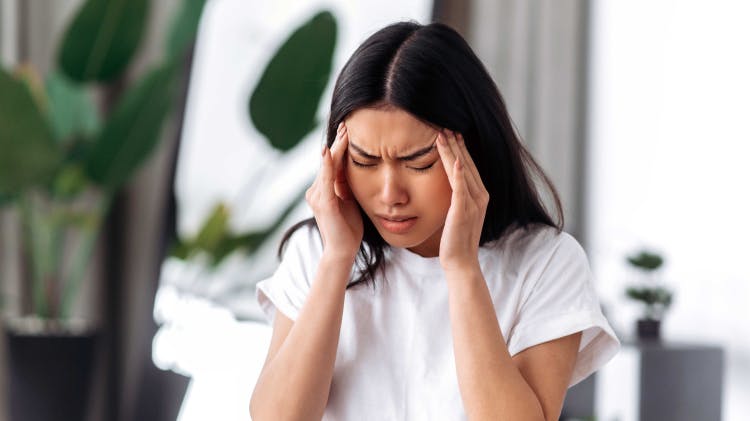 Νεαρή ασθενής κάνει μορφασμούς και τρίβει τους κροτάφους της καθώς υποφέρει από ημικρανία