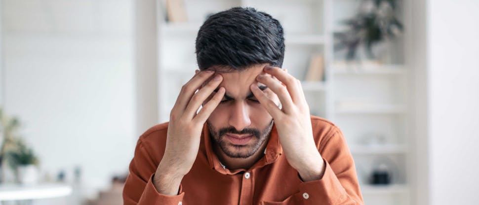 Ένας νεαρός ασθενής φορά ένα πορτοκαλί πουκάμισο ενώ κάθεται στο διαμέρισμά του ή στο γραφείο του. Κλείνει τα μάτια του και τρίβει τους κροτάφους του σαν να υποφέρει από πονοκέφαλο ή ημικρανία.