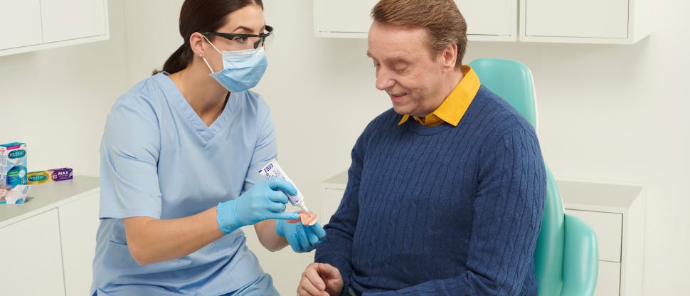 Εικόνα νεαρής οδοντιάτρου που δείχνει τη χρήση στερεωτικής κρέμας για οδοντοστοιχίες σε ασθενή που φοράει οδοντοστοιχία