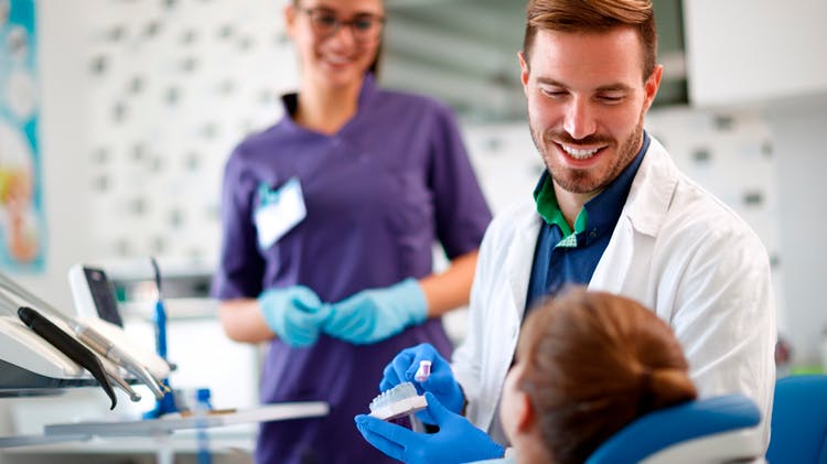 A dentist shows a happy women how to brush with a mouth model