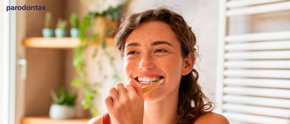 Young woman smiling while brushing her teeth in bathroom mirror