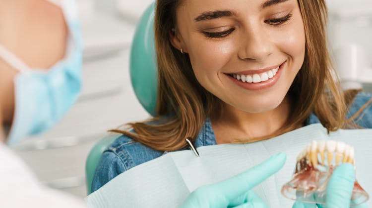 A dentist shows a happy woman how to brush her teeth with a mouth model