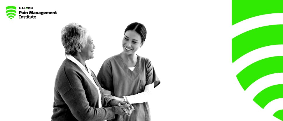 Young female healthcare professional smiles as she speaks to an older female patient and leads her by the arm