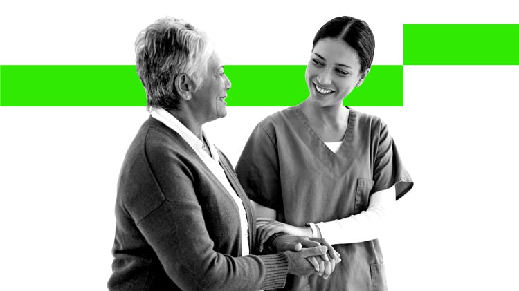 Young female healthcare professional smiles as she speaks to an older female patient and leads her by the arm