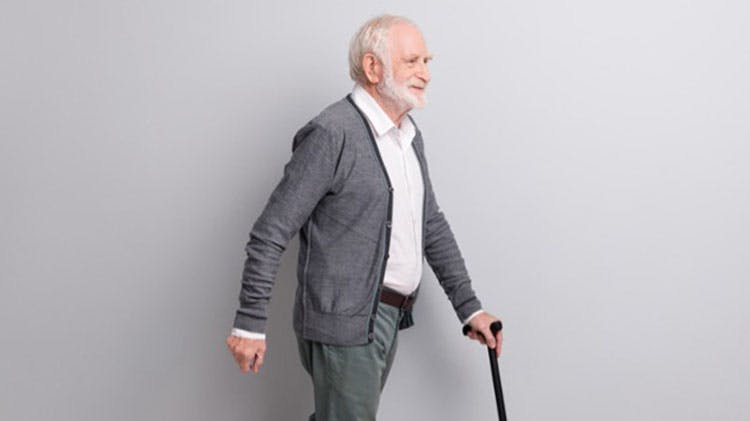 Grey-haired man smiling and walking with a stick