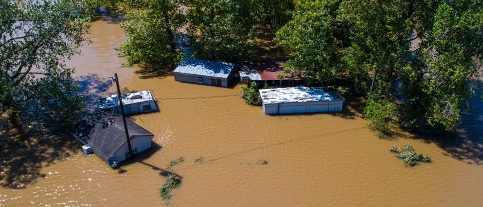 Aerial image of a flooded town, with brown water encircling 5 homes and buildings