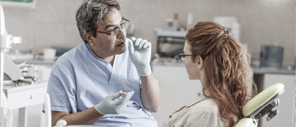 Dentist talking to patient about dentine hypersensitivity (tooth sensitivity)