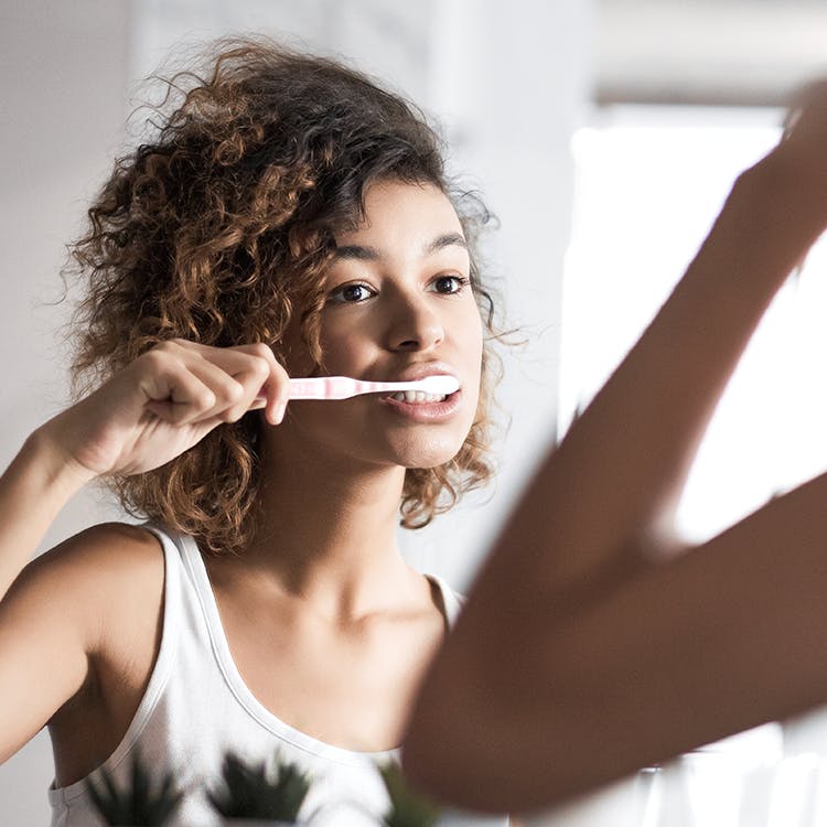 Woman brushes her teeth in a mirror.