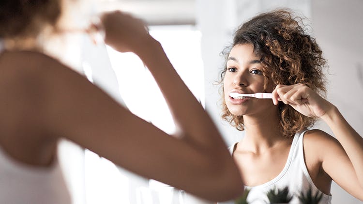 Woman brushes her teeth in a mirror.