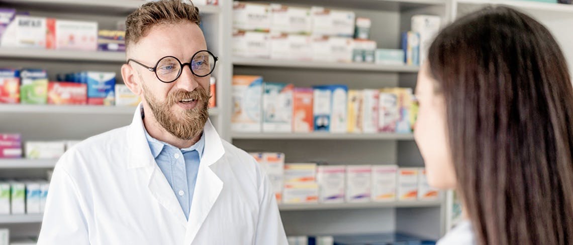 Pharmacist behind the counter speaking to a patient