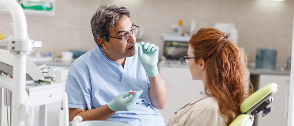Male orthodontist with glasses conversing with female patient as she sits in the appointment chair