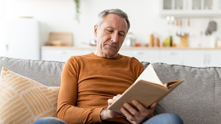 Older man on a sofa reading a book