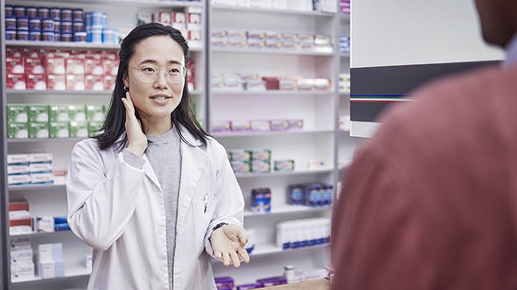 Young pharmacist talking to patient about pain management while stood behind her pharmacy counter