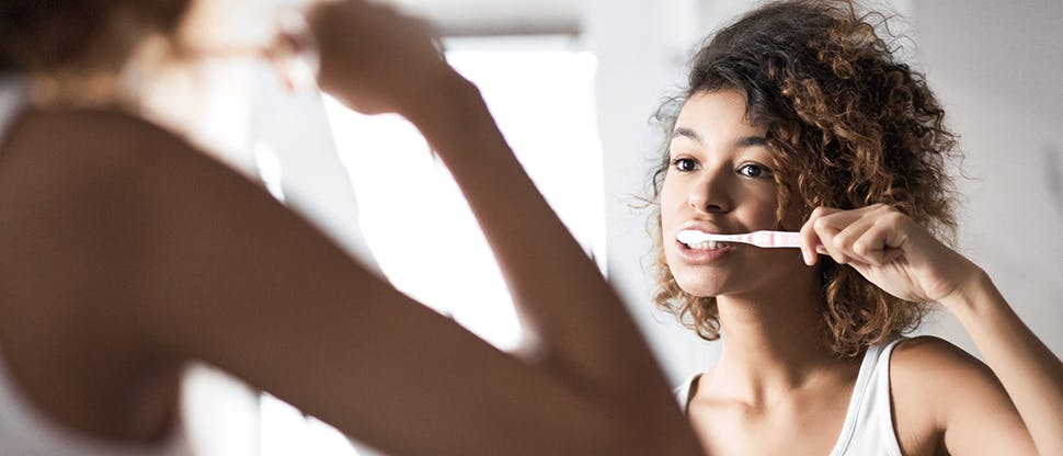 Woman brushes her teeth in a mirror.