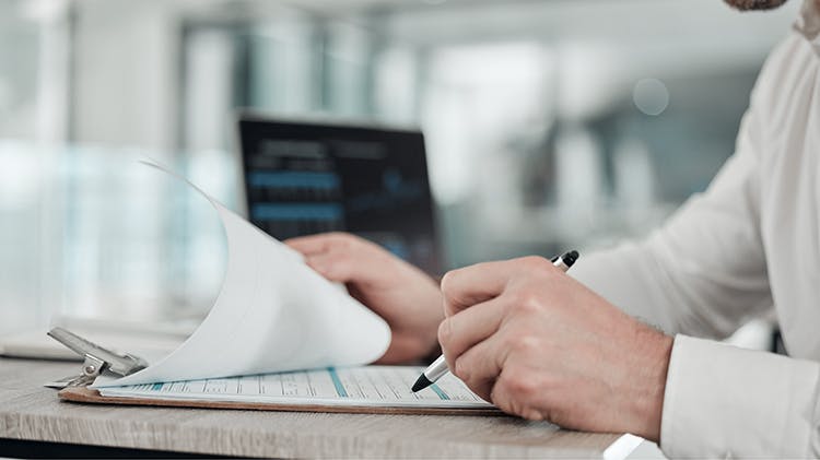 Image of a pharmacist siting at a desk, reviewing documents on a clipboard