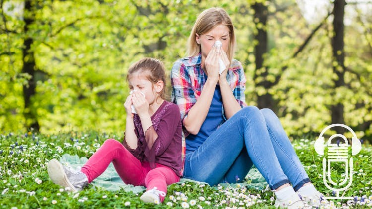 Woman and child sitting on grass spotted with daisy’s both blowing their noses