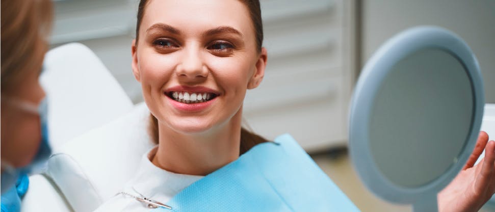 Dentist using tools in patient’s mouth while patient holds up a mirror to see their teeth