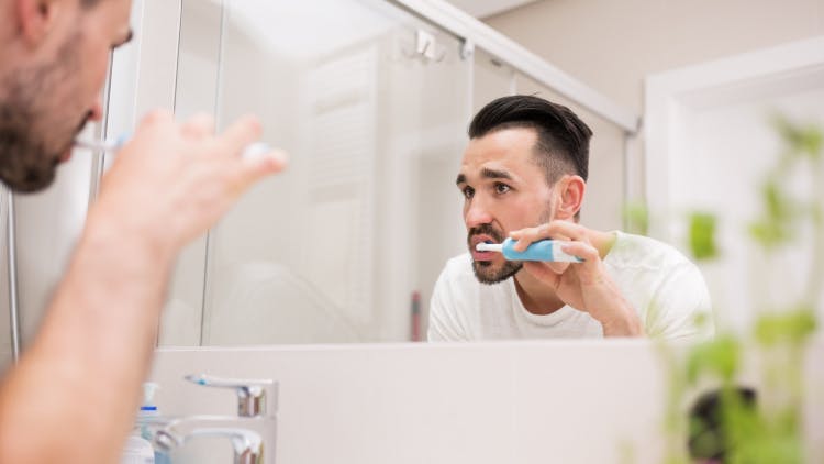 A man brushing his teeth with a daily fluoride toothpaste such as corsodyl.