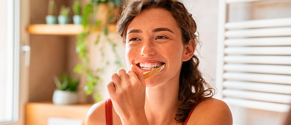 Young woman smiling while brushing her teeth in bathroom mirror