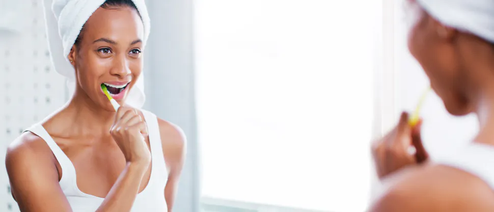 Young woman smiling while brushing her teeth in bathroom mirror