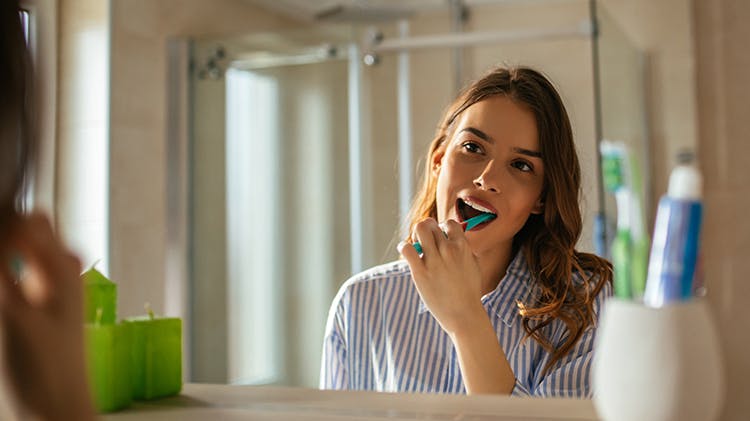 Woman looking in mirror brushing teeth