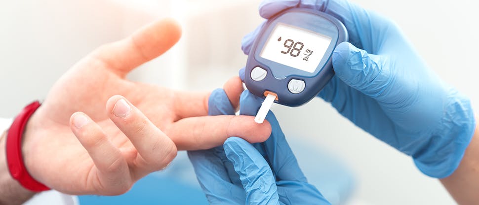 The gloved hand of a healthcare professional performs a finger prick test on a patient.