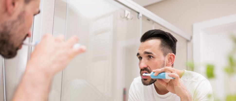 Young man looking in the mirror while brushing his teeth