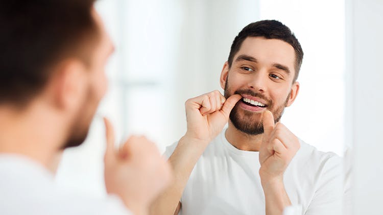 Man looking in mirror flossing teeth