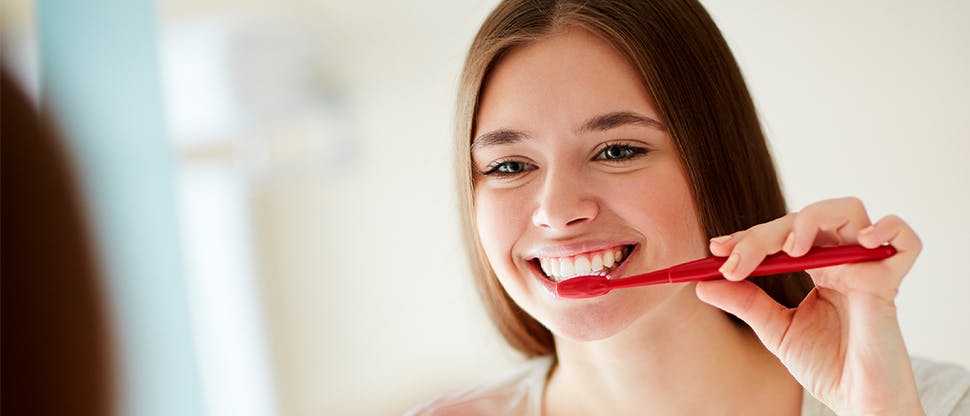 A young woman brushes her teeth to help maintain good gum health.
