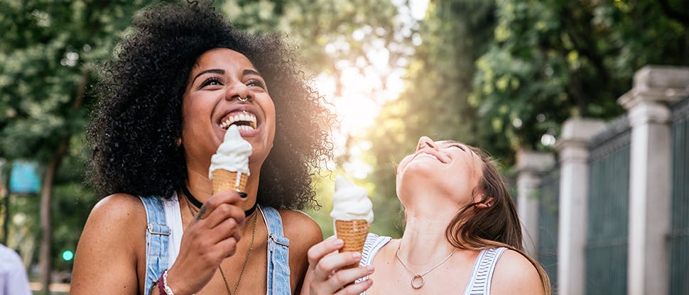 Two young women enjoy a cold icecream in the park, free from tooth sensitivity pain.