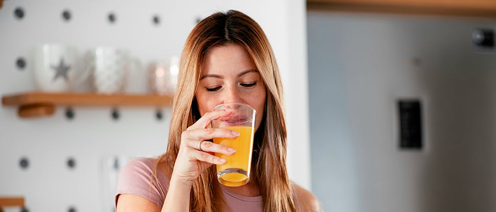 A woman drinks an acidic orange drink, possibly causing tooth enamel wear. 