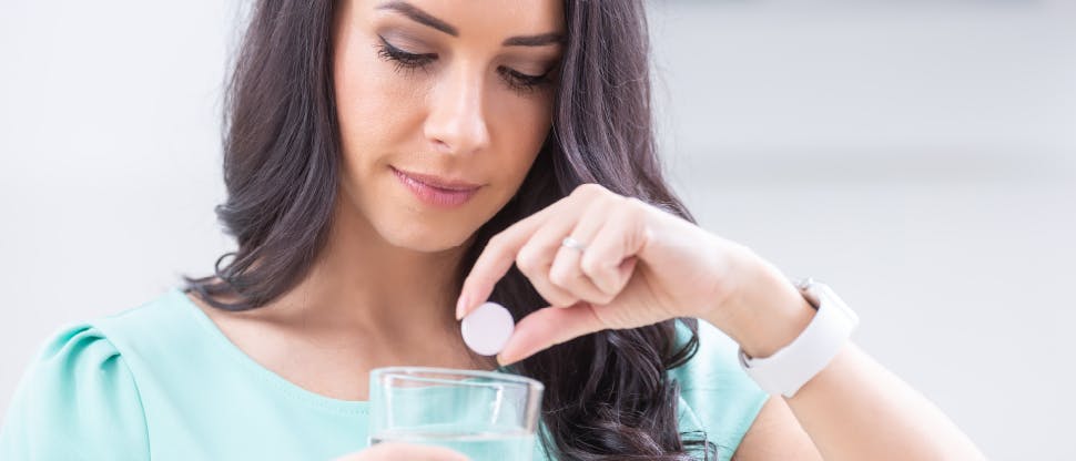 mage of woman dropping a soluble tablet into a glass of water