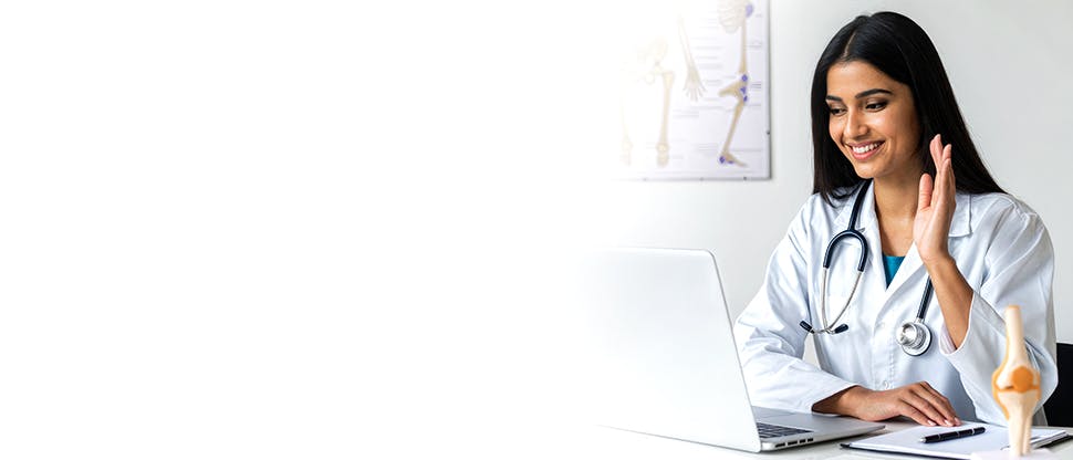 Female doctor working at laptop in hospital office, on a video conference call.