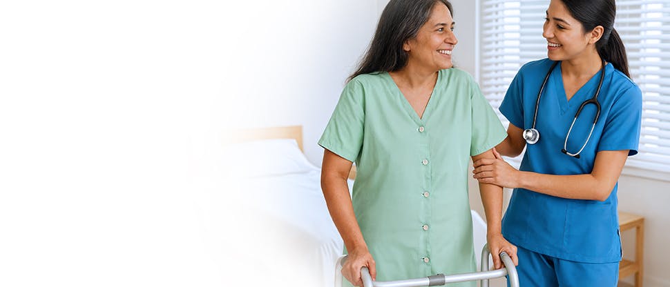 A female doctor helping a female patient wearing a hospital gown with physical exercise.