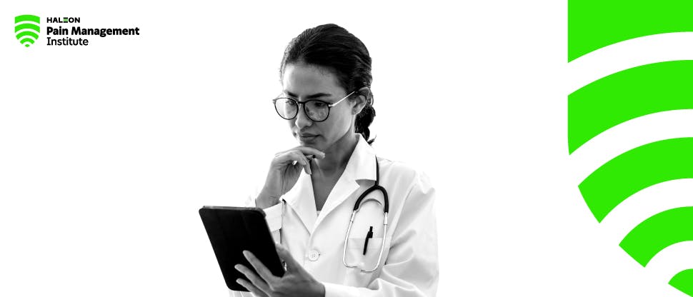 A young female doctor looks down at a tablet computer with a look of concentration.