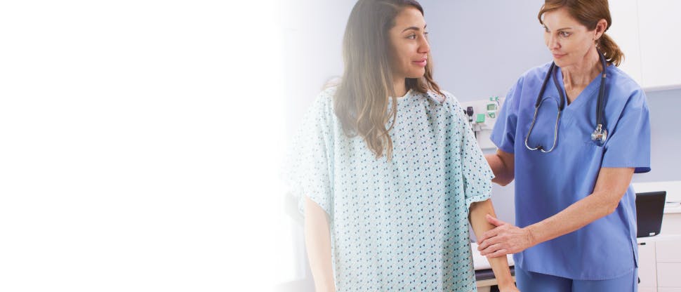 A female doctor helping a female patient wearing a hospital gown with physical exercise.