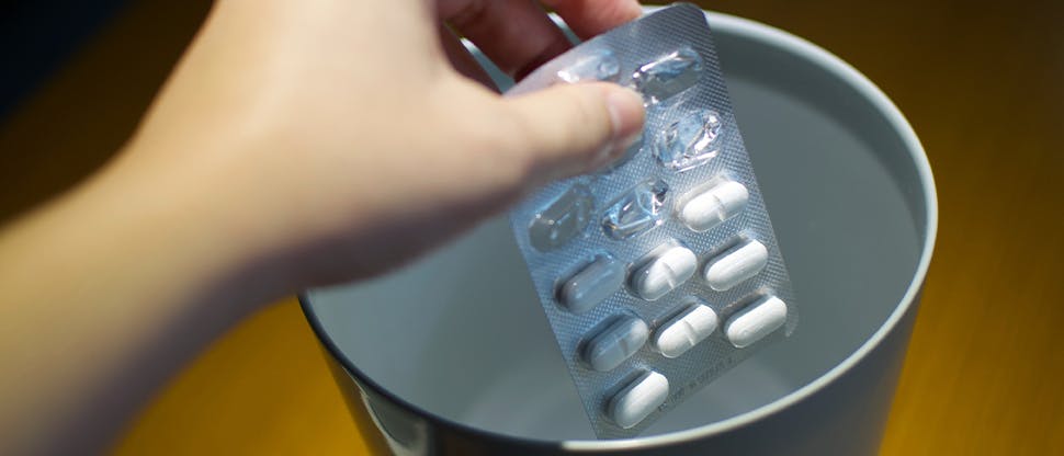 A hand places an expired pill packet in a safe disposal area to dispose of the medicine safely and correctly.