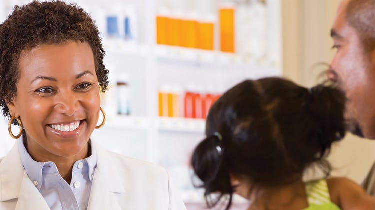 A pharmacist smiling at a young child and her parent