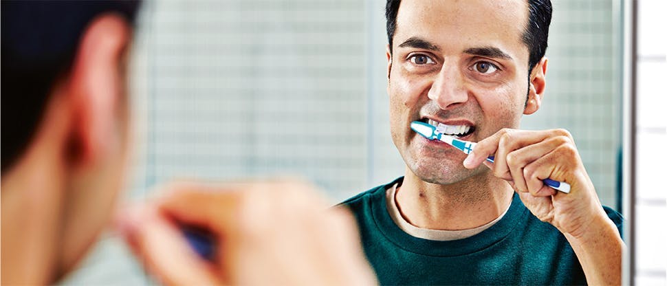 A man brushes his teeth with a fluoride and sodium bicarbonate toothpaste such as parodontax to help remove plaque.