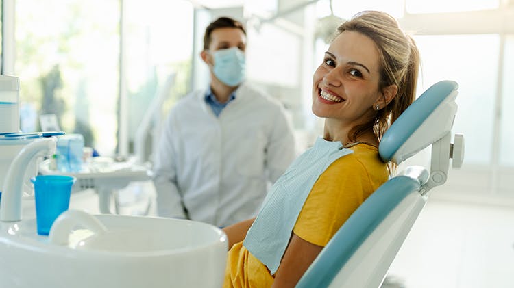Woman in glasses sits in dental chair and looks out smiling wide
