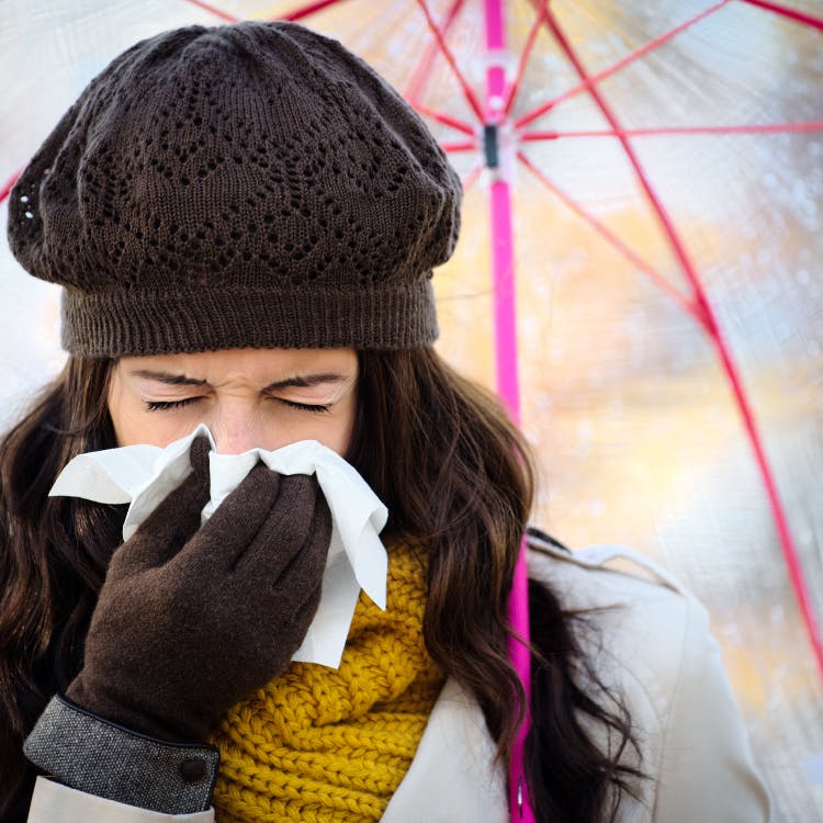 Lady under an umbrella with tissue to her nose