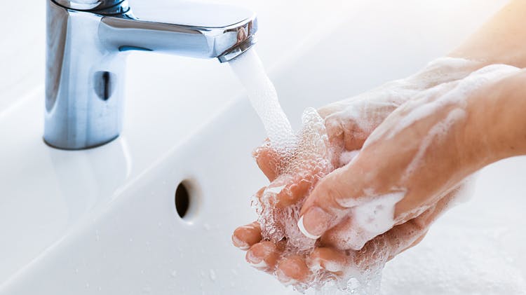 Woman with manicured nails washes her hands in a sink