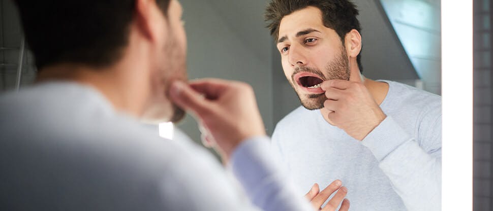 A man examines his inner mouth in the bathroom mirror searching for signs of gingivitis or gum disease.